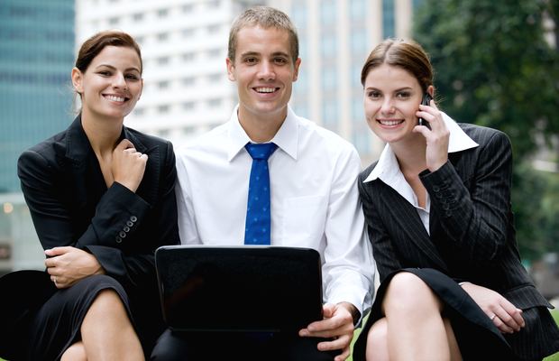 Three colleagues sit outside an office with a laptop and a phone