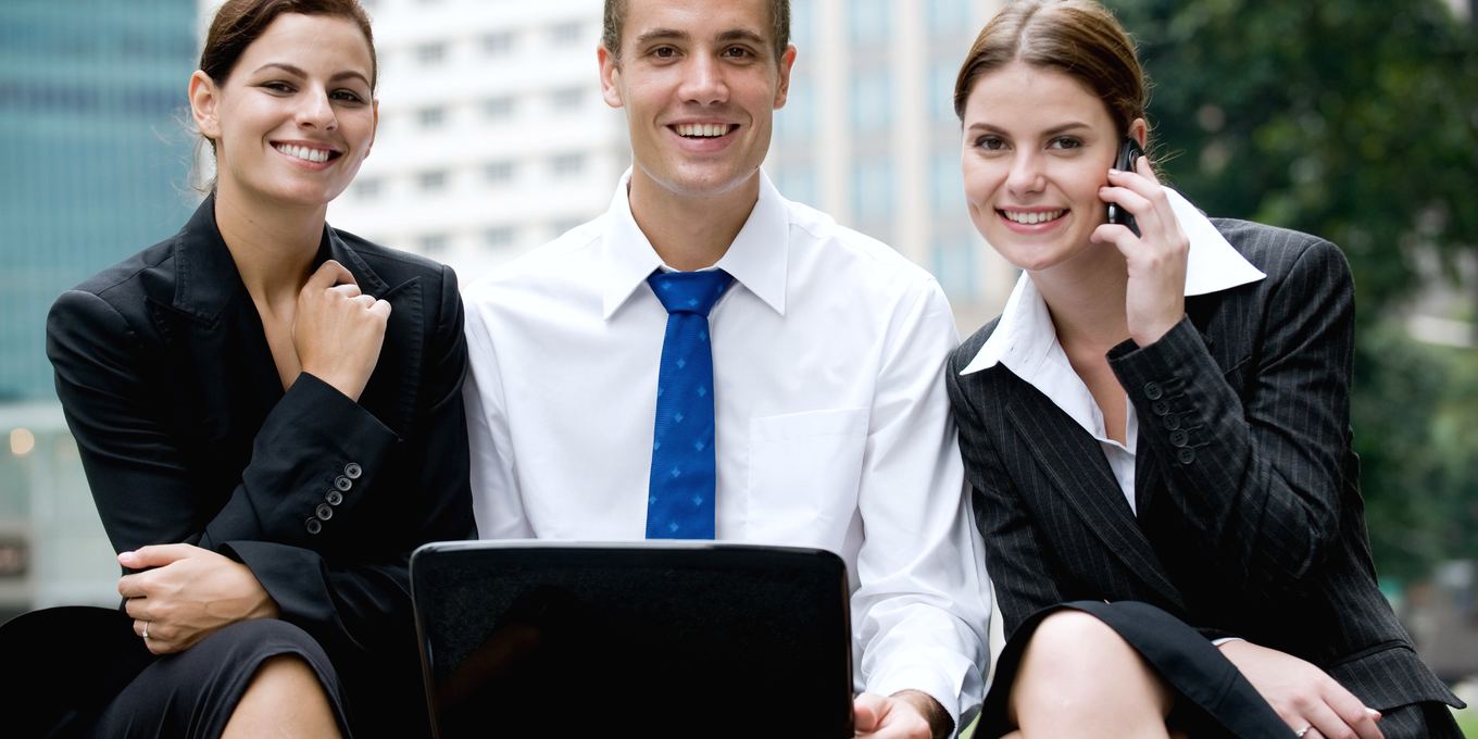 Three colleagues sit outside an office with a laptop and a phone