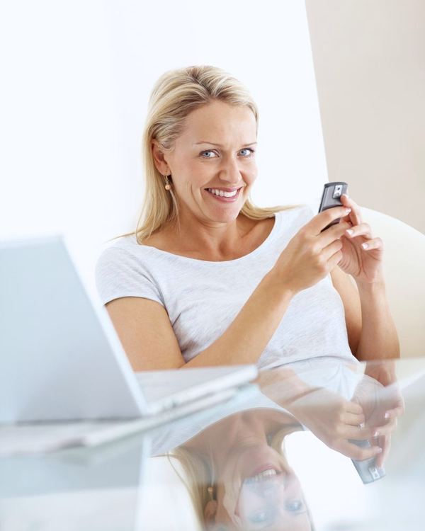 A woman at a desk smiles as she reads a text message on her phone