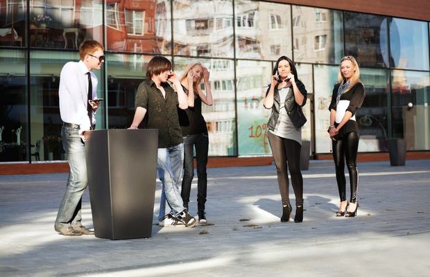 A group of young friends stand outside, each using a mobile phone