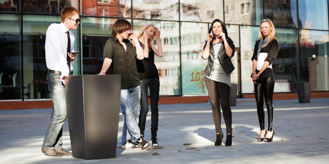 A group of young friends stand outside, each using a mobile phone