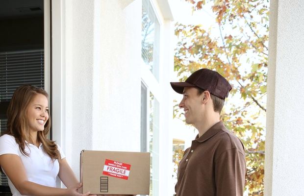 A courier with a parcel smiles at a woman opening her front door