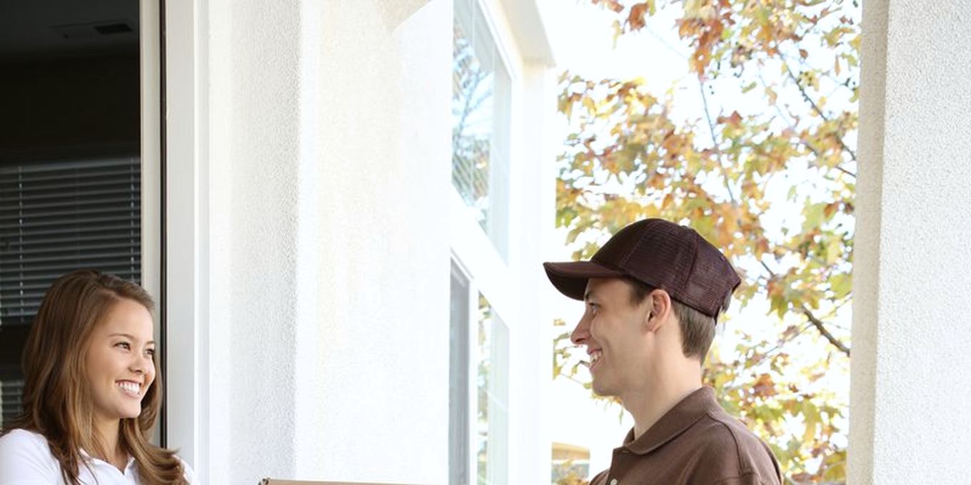 A courier with a parcel smiles at a woman opening her front door